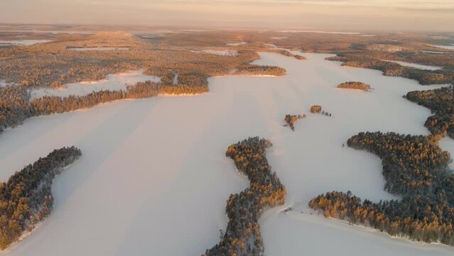 Winter in Finland; slow forward drone flight over a snow covered landscape with boreal forests and frozen lakes in southern Lapland at sunrise