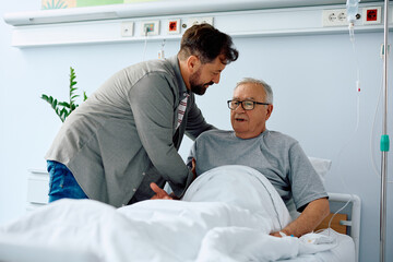Caring son helps his hospitalized senior father to get up from bed.