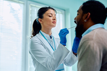 Female doctor examining throat of black man during appointment at medical clinic.