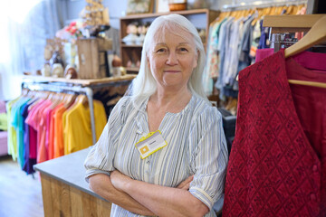 Portrait Of Senior Female Volunteer Working In Charity Shop Or Thrift Store Selling Used And...