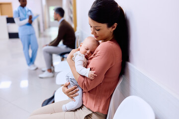 Caring mother holds her sleepy baby in waiting room at doctor's office.