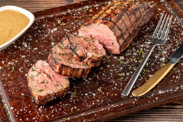 Sliced grilled beef tenderloin seasoned with salt, rosemary and thyme on a wooden cutting board