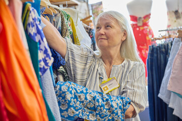 Senior Female Volunteer Working In Charity Shop Or Thrift Store Selling Used And Sustainable...