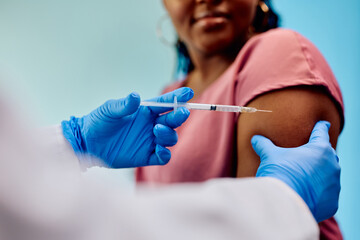 Close up of doctor giving vaccine to black woman at clinic.