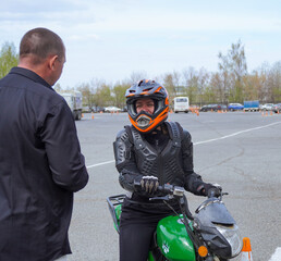A young woman is learning to ride a motorbike in a motorcycle school. She is taught by a teacher