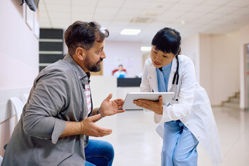 Obraz premium Japanese doctor and her male patient talk while using touchpad at clinic.