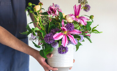 A man in an apron holds a vase of flowers, close-up.