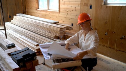 Female mechanical engineer with hard hat doing walkthrough inspection of new house construction with blueprints.