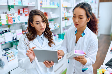 Fototapeta na wymiar Female pharmacists cooperate while using touchpad and working in drugstore.