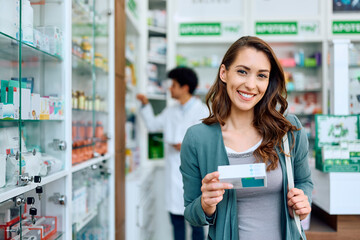 Young happy woman buying medicine in pharmacy and looking at camera.