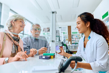 Happy Chinese pharmacist assists her senior customers in buying medicine in pharmacy.