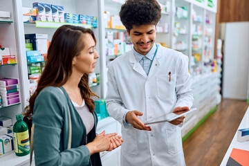 Obraz premium Happy pharmacist and his female customer using touchpad in pharmacy.