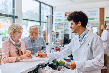 Fototapeta na wymiar Happy pharmacist gives prescription medicine to senior couple in pharmacy.