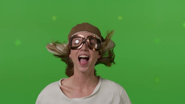 Close-up of a girl's face in a retro pilot's hat blown by a strong wind on Green screen background, chroma key.