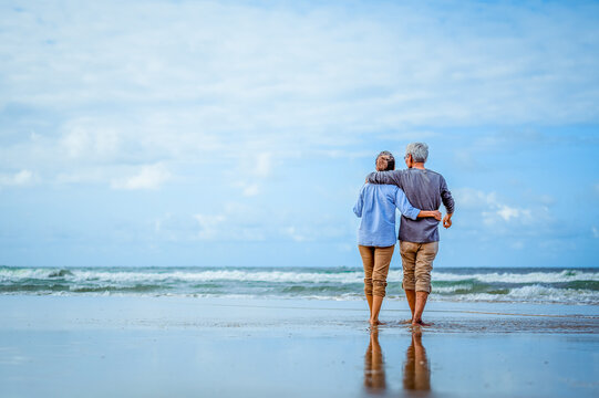 Plan life insurance of happy retirement concepts. Senior couple walking on the beach holding hands at beach sunrise in evening.