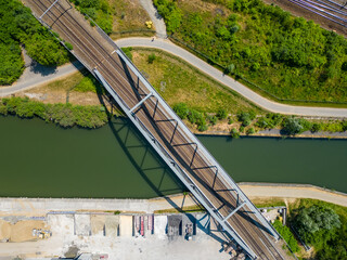 Aerial view of metal railway bridge over the water of a river, with the forest and field aside it. Top view of railroad from drone. High quality photo