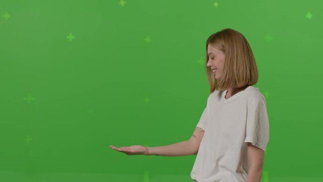 Young caucasian woman holding something imaginary with hands, showing a product, smiling and cheerful, offering an imaginary object on a Green Screen, Chroma Key background. 4k UHD footage video