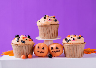 Halloween cupcakes with orange cream and festive sugar sprinkles: bats and eyes, and pumpkin sweets on purple background. Holiday desserts