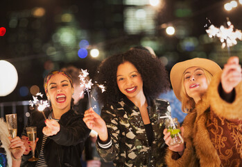 Portrait enthusiastic young women waving sparklers at party
