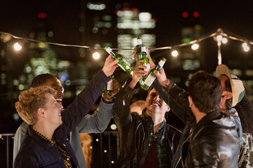 Young men toasting beer bottles at rooftop party