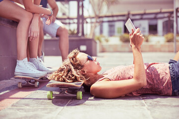 Young woman with digital tablet laying on skateboard - obrazy, fototapety, plakaty