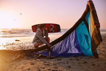 Man with kiteboarding equipment on sunset beach