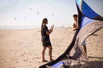 Woman instructing man with kiteboarding kite on sunny beach