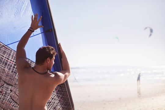 Man Lifting Kiteboarding Kite On Sunny Beach