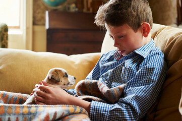 Boy holding puppy in lap on sofa © KOTO