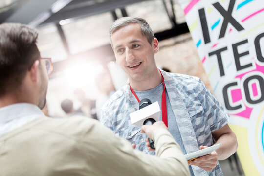Speaker with microphone interviewing man at technology conference