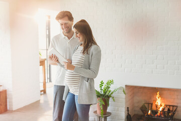 Pregnant couple using digital tablet near fireplace