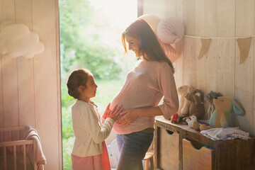 Daughter touching pregnant mother's stomach in nursery - obrazy, fototapety, plakaty