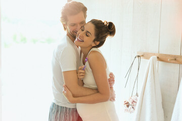 Affectionate pregnant couple hugging in sunny bathroom
