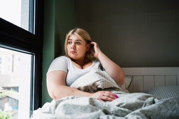 Unhappy sad depressed lonely plus size overweight woman looks at window and thinks about problems....