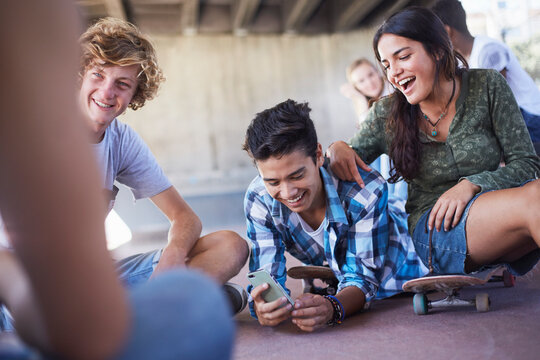 Teenage friends hanging out texting with cell phone at skate park