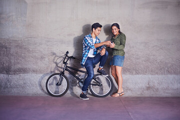 Teenage couple with BMX bicycle texting at wall
