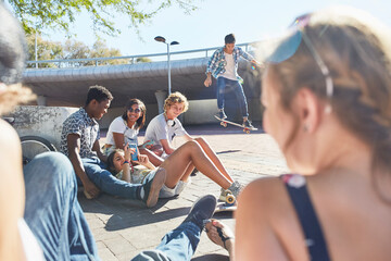 Teenage friends hanging out skateboarding at sunny skate park