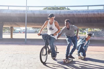 Deurstickers Teenage boys riding BMX bicycle and skateboarding at sunny skate park © KOTO