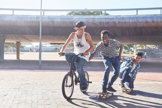 Teenage boys riding BMX bicycle and skateboarding at sunny skate park