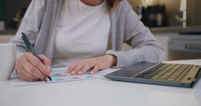 Female typing on keyboard and records the financial report in work papers at workplace home office. Attractive business girl manager uses laptop for checking financial statements, working freelance