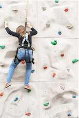 Teenage teen girl grabbing artificial high climbing wall with split ledges. Climbing harness safety...
