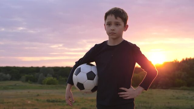 Portrait of a boy on the background of sunset. A kid holds a soccer ball and looks at the camera. The child dreams of becoming a football player.