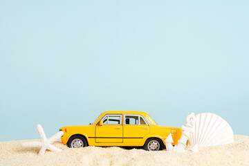 Toy taxi car with seashells on beach sand, blue background. taxi booking service. Travel. Summer...