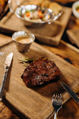 Fresh juicy delicious beef steak on wooden background in restaurant. Meat dish with spices and herbs