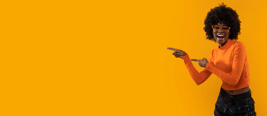 Positive woman with afro hairstyle pointing on yellow background.