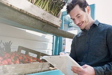 Smiling farmer's market worker checking inventory clipboard next to strawberries