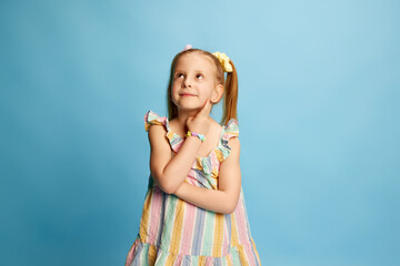 Portrait of cute, beautiful little girl, child standing with calm, dreamy face against blue studio...