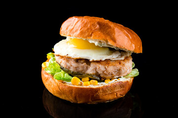 Pork burger with fried eggs, corn, pickles, lettuce and sauce, American cuisine.