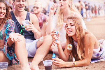 Young friends hanging out blowing bubbles at music festival