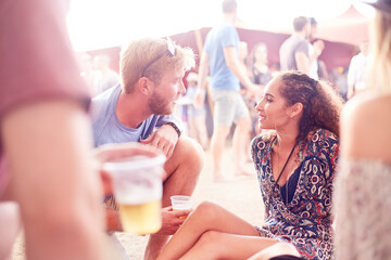 Young couple drinking beer and talking at music festival